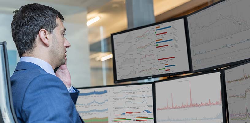 Man looking at multiple computer screens with analytic dashboards
