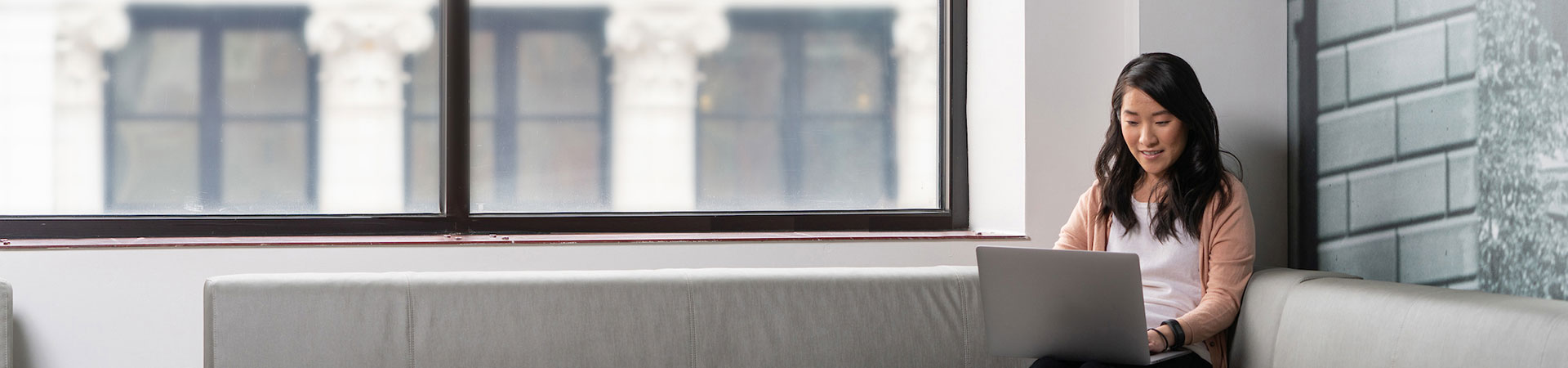 Frau sitzt auf Couch im Büro und schaut auf ihren Laptop